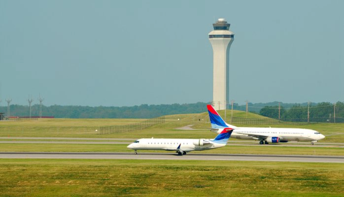Two airplanes taxiing next to a control tower